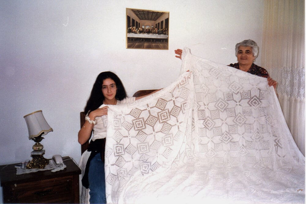 Ariane and her nonna are holding up a lace tablecloth.