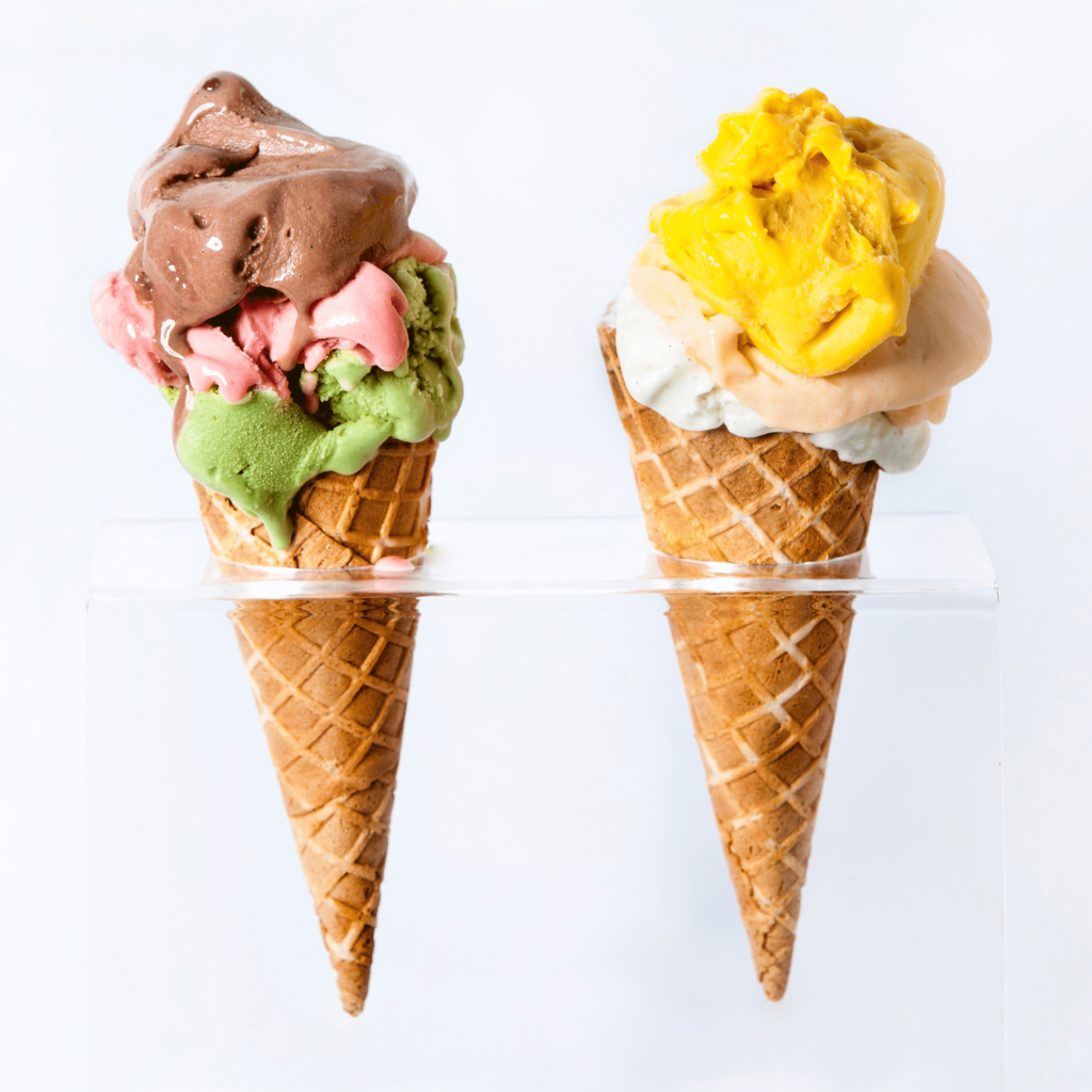 2 gelato cones with triple scoops that are place on a transparent stand